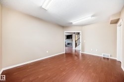 Spacious room featuring wood-finish flooring, light beige wall paint, white trim, and two overhead fluorescent light fixtures - 