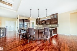 Open-concept kitchen featuring dark wood cabinetry, stainless steel appliances, a tile backsplash, a large island with a breakfast bar, and wood-finish flooring - 