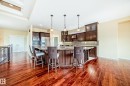 Open-concept kitchen featuring dark wood cabinetry, stainless steel appliances, a tile backsplash, a large island with a breakfast bar, and wood-finish flooring - 527 Callaghan Point(E), Edmonton, AB  - Indoor 