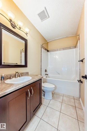 Bathroom featuring a single vanity with a laminate countertop, a framed mirror, a three-light fixture, a white toilet, and a shower-tub combination with tile surround - 527 Callaghan Point(E), Edmonton, AB - Indoor Photo Showing Bathroom