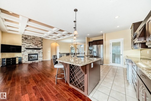Open-concept kitchen and living area featuring a central island with integrated wine rack, stainless steel appliances, and rich wood-finish flooring - 527 Callaghan Point(E), Edmonton, AB - Indoor Photo Showing Kitchen With Fireplace With Upgraded Kitchen
