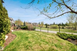 Landscaped backyard featuring a manicured lawn, established shrubbery, a black metal fence, and a paved pathway beyond the property line - 
