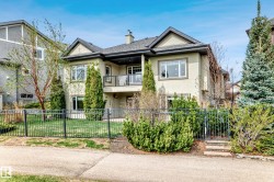 Multi-level stucco exterior featuring a second-story balcony with glass railing, multiple windows, and a fenced backyard with mature landscaping - 