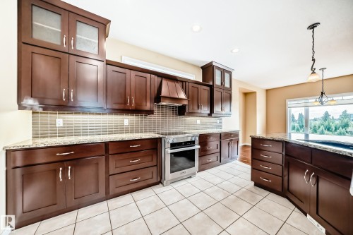 Modern kitchen featuring dark wood-finish cabinetry, granite countertops, and a full-height tiled backsplash - 527 Callaghan Point(E), Edmonton, AB - Indoor Photo Showing Kitchen