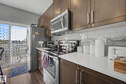 Modern kitchen featuring wood-finish cabinetry, stainless steel appliances, white subway tile backsplash with glass accent, and light-toned countertops - 17 320 Secord Boulevard, Edmonton, AB - Indoor Photo Showing Kitchen