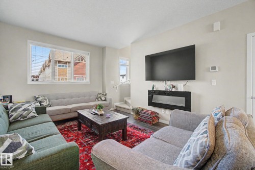 Spacious living area featuring light-colored walls, wood-finish flooring, and a large window with blinds - 17 320 Secord Boulevard, Edmonton, AB - Indoor Photo Showing Living Room With Fireplace