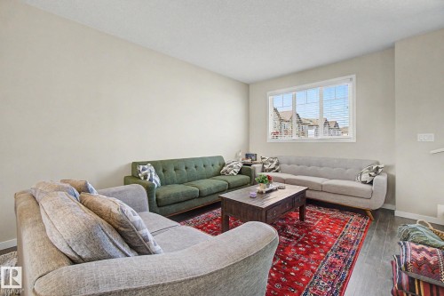 Spacious living area featuring light-toned walls, wood-finish flooring, and a large window with white blinds - 17 320 Secord Boulevard, Edmonton, AB - Indoor Photo Showing Living Room