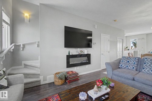 Living area featuring wood-finish flooring, a wall-mounted electric fireplace, and a staircase with carpeted treads and a white handrail - 17 320 Secord Boulevard, Edmonton, AB - Indoor Photo Showing Living Room With Fireplace