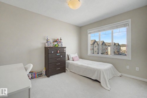 Bright room featuring a large multi-pane window, neutral-toned walls, and light-colored carpet flooring - 17 320 Secord Boulevard, Edmonton, AB - Indoor Photo Showing Bedroom