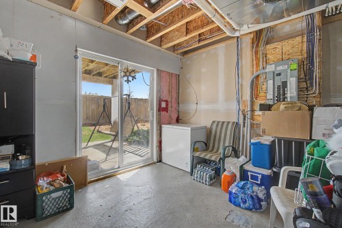 Unfinished basement space featuring exposed ceiling joists and ductwork, a sliding glass door providing exterior access, and a concrete floor - 17 320 Secord Boulevard, Edmonton, AB - Indoor Photo Showing Other Room