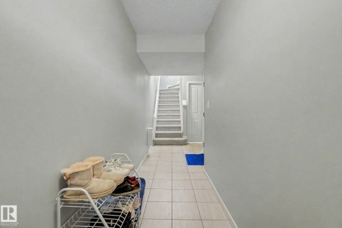 Hallway featuring light-toned tile flooring, light gray painted walls, and a staircase with light-toned carpeted treads - 17 320 Secord Boulevard, Edmonton, AB - Indoor Photo Showing Other Room