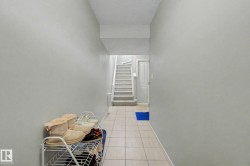 Hallway featuring light-toned tile flooring, light gray painted walls, and a staircase with light-toned carpeted treads - 