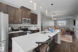 Modern kitchen featuring a white countertop island with an undermount sink, dark wood-finish cabinetry, stainless steel appliances, and a subway tile backsplash - 