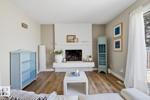 Living area featuring a white-painted brick fireplace with a hearth, wood-finish flooring, and a sliding glass door - 17604 85 Avenue, Edmonton, AB - Indoor Photo Showing Living Room With Fireplace