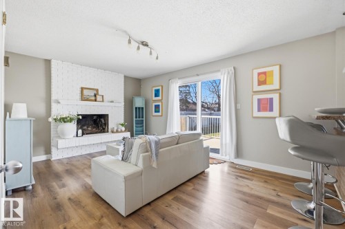 Living area featuring a white brick fireplace with mantel, wood-finish flooring, and track lighting - 17604 85 Avenue, Edmonton, AB - Indoor Photo Showing Living Room With Fireplace