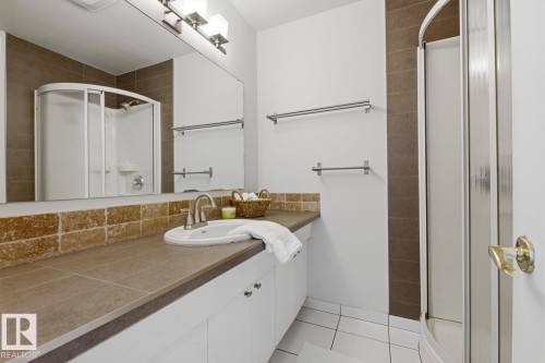 Bathroom featuring a white vanity with an integrated sink, a rectangular mirror, and a curved glass-enclosed shower - 17604 85 Avenue, Edmonton, AB - Indoor Photo Showing Bathroom