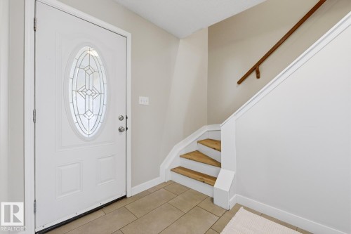 Entryway featuring a white paneled door with an oval decorative glass insert, neutral-toned wall paint, light-toned tile flooring, and a staircase with natural wood treads and a wood handrail - 17604 85 Avenue, Edmonton, AB - Indoor Photo Showing Other Room