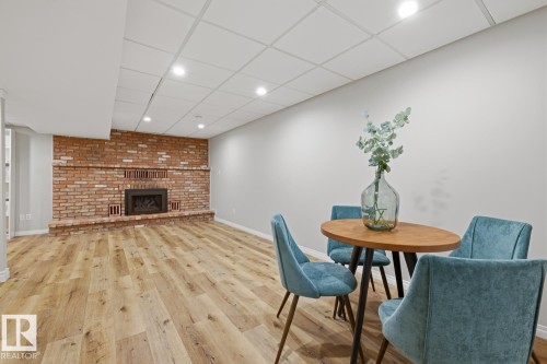 Spacious room featuring a prominent brick-faced fireplace with a black insert, wood-finish flooring, and recessed ceiling lighting - 17604 85 Avenue, Edmonton, AB - Indoor Photo Showing Other Room With Fireplace