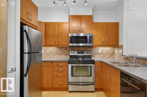 U-shaped kitchen featuring wood-finish cabinetry, stainless steel appliances, and a tiled backsplash - 223 10121 80 Avenue, Edmonton, AB - Indoor Photo Showing Kitchen With Stainless Steel Kitchen With Double Sink