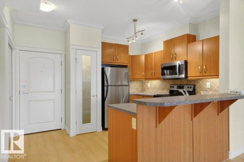 Kitchen featuring light wood-finish cabinetry, stainless steel appliances, and a breakfast bar. - 223 10121 80 Avenue, Edmonton, AB - Indoor Photo Showing Kitchen