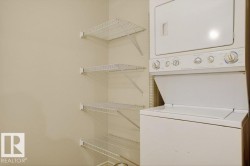 Laundry room featuring a stacked washer and dryer unit and multiple wire shelving units. - 