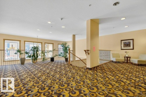 Spacious upper-level landing with patterned carpet flooring, recessed lighting overlooking the main entrance below. - 223 10121 80 Avenue, Edmonton, AB - Indoor Photo Showing Other Room