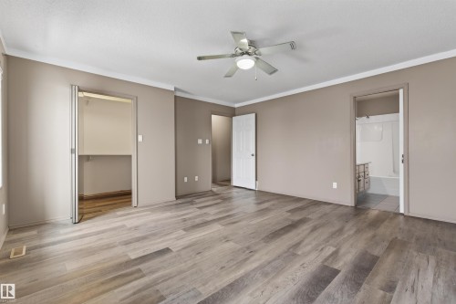 Spacious room featuring wood-finish flooring, a ceiling fan with integrated lighting, bi-fold closet doors, and access to an en-suite bathroom with a built-in vanity and tub/shower combination - 3917 52 Avenue, Cold Lake, AB - Indoor Photo Showing Other Room