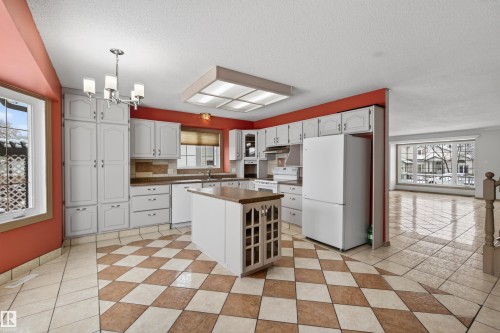 Spacious kitchen featuring an island with a wood-finish countertop, checkerboard tile flooring, white cabinetry, and white appliances - 3917 52 Avenue, Cold Lake, AB - Indoor Photo Showing Kitchen