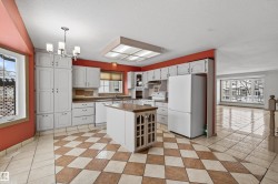 Spacious kitchen featuring an island with a wood-finish countertop, checkerboard tile flooring, white cabinetry, and white appliances - 