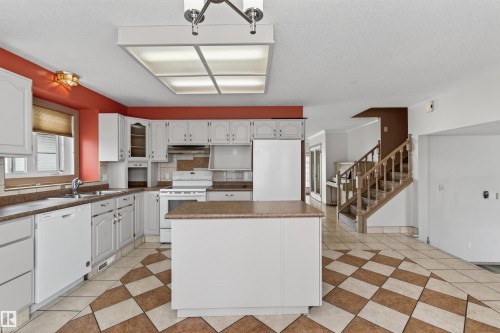 Spacious kitchen featuring white cabinetry, a central island, integrated appliances, and checkered tile flooring - 3917 52 Avenue, Cold Lake, AB - Indoor Photo Showing Kitchen With Double Sink