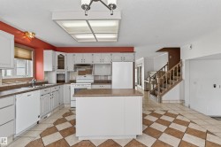 Spacious kitchen featuring white cabinetry, a central island, integrated appliances, and checkered tile flooring - 