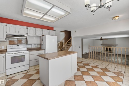 Kitchen featuring white cabinetry, a built-in range, a matching refrigerator, a center island with a countertop, and checkerboard floor tiling - 3917 52 Avenue, Cold Lake, AB - Indoor Photo Showing Kitchen