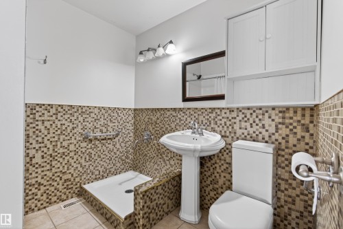 Bathroom featuring a pedestal sink, walk-in shower with grab bar, mosaic tile surround, and white wall-mounted cabinetry - 3917 52 Avenue, Cold Lake, AB - Indoor Photo Showing Bathroom