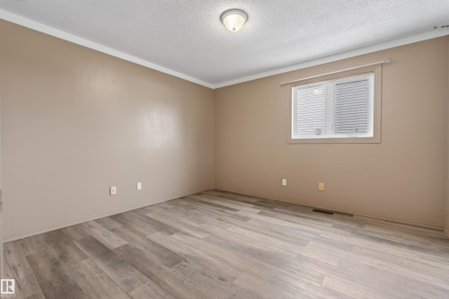 Spacious room featuring wood-finish flooring, neutral-toned walls, white crown molding, and a window with blinds - 3917 52 Avenue, Cold Lake, AB - Indoor Photo Showing Other Room