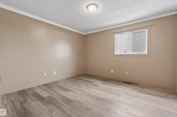Spacious room featuring wood-finish flooring, neutral-toned walls, white crown molding, and a window with blinds - 