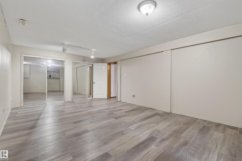Spacious room featuring wood-finish flooring, mirrored closet doors, and track lighting - 3917 52 Avenue, Cold Lake, AB - Indoor Photo Showing Other Room