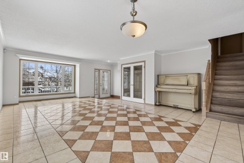Spacious open room featuring a large bay window, checkered tile flooring, a chandelier, French doors, and a wood staircase - 3917 52 Avenue, Cold Lake, AB - Indoor
