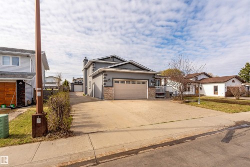 Contemporary two-story residence featuring a two-car garage, gray stucco siding, stone accents, and a long concrete driveway leading to an additional detached garage - 3917 52 Avenue, Cold Lake, AB - Outdoor With Facade