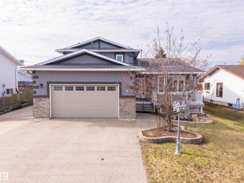 Contemporary home exterior featuring a two-car garage with transom windows, a multi-tiered roofline, a front deck with white railings, brick accents, and a paved driveway - 3917 52 Avenue, Cold Lake, AB - Outdoor