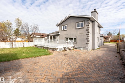 Rear exterior featuring a spacious paver driveway, an expansive white deck, a stucco finish, and a grass lawn - 3917 52 Avenue, Cold Lake, AB - Outdoor With Deck Patio Veranda