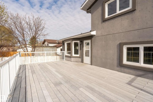 Expansive wood-finish deck with white railing, featuring a stucco exterior with multiple windows and an exterior door - 3917 52 Avenue, Cold Lake, AB - Outdoor With Exterior