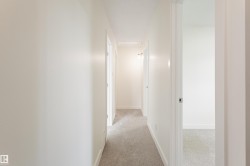 Hallway with light gray carpet flooring, white walls, and white trim - 