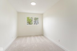 Bright interior room featuring a window with exterior tree scenery, light neutral carpeting, white baseboards, and a contemporary ceiling light fixture - 