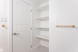 Built-in shelving for storage, modern interior door with brushed nickel hardware, light gray tile flooring, and a brass wall-mounted towel bar - 