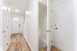 Entryway featuring wood-finish flooring, a white paneled door with an arched window, a ceiling light fixture, and an additional white door with brass hardware - 