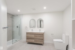 Modern bathroom featuring a frameless glass shower enclosure with subway tile surround, a dual vanity with wood-finish cabinetry, twin arched mirrors, and recessed lighting - 