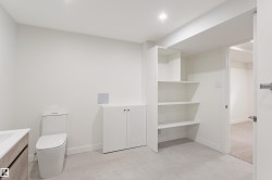 Contemporary bathroom featuring a modern toilet, light wood-finish vanity with an integrated sink, built-in open shelving, and additional cabinet storage, all complemented by light grey tile flooring - 