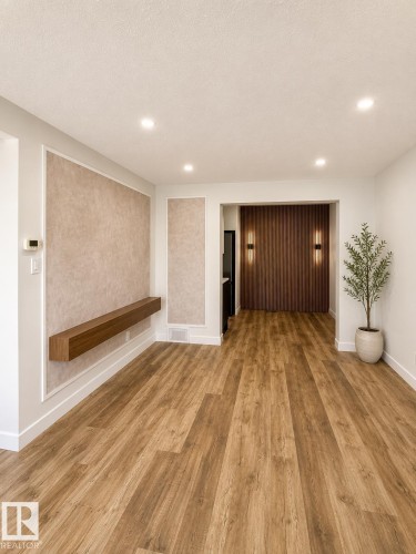 Spacious living area featuring wood-finish flooring, recessed lighting, and a decorative wall panel with a floating wood shelf - 224 Callingwood Two Two, Edmonton, AB - Indoor Photo Showing Other Room