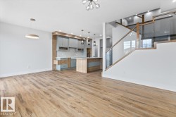 Spacious open-concept living area featuring wood-finish flooring, a contemporary kitchen with a center island, and a modern glass-paneled staircase with wood handrails - 