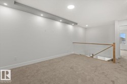 Upper-level landing featuring carpeted flooring, a glass and wood railing, recessed ceiling lighting, and a contemporary light fixture - 